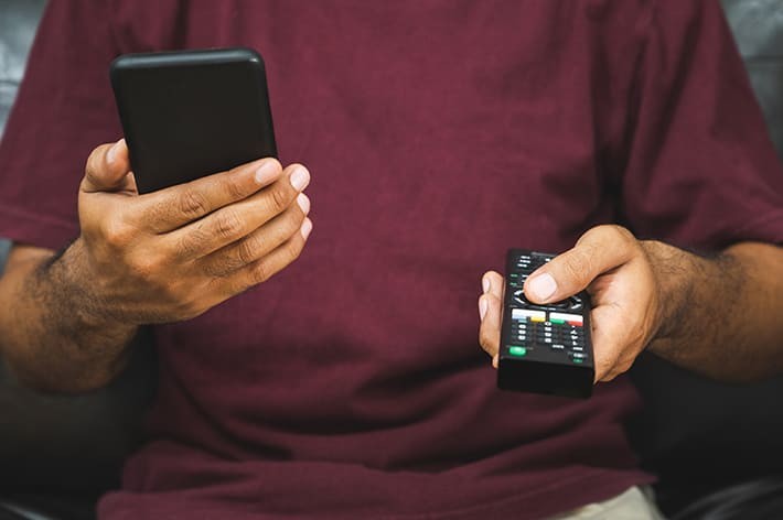 テレビリモコンとスマホを持つ男性